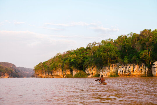 Unrecognizable fisherman on rowboat in moody river sorrounded by jungle and rocky landscape