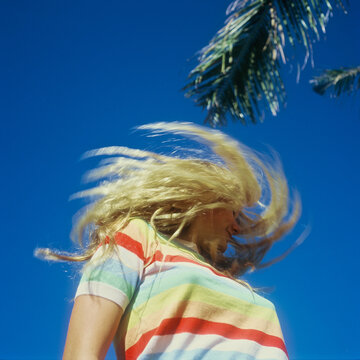 blonde teenage girl in rainbow sweater against bright blue sky