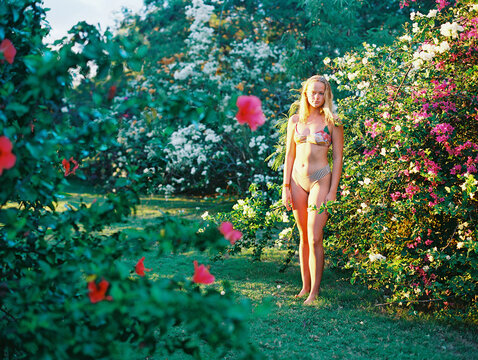 blonde teenager in bikini standing in flowering garden bushes