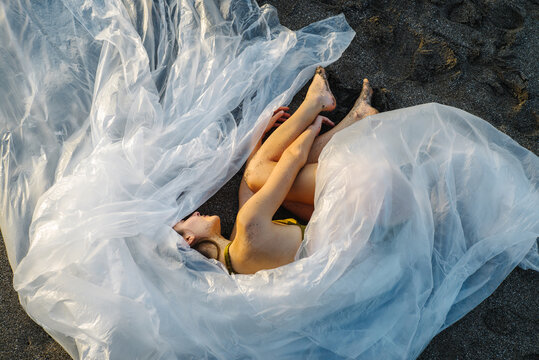 The girl is wrapped in plastic film and lies on the black sand on the beach