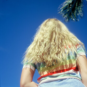 blonde teenage girl in rainbow sweater against bright blue sky