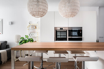 Modern dining room with two pendant lamps over dining table, chairs and oven