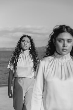 two fashionable women wearing similar outfits standing on a sunny ferry deck