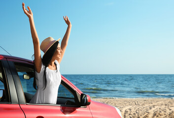Fototapeta premium Happy young woman leaning out of car window on beach, space for text. Summer trip