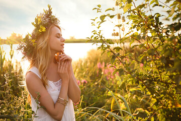 Young woman wearing wreath made of beautiful flowers outdoors on sunny day