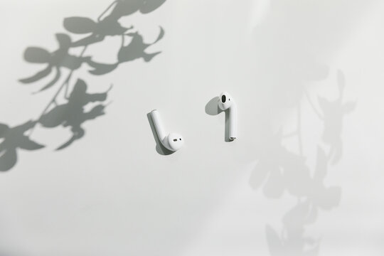 wireless headphone air pods on white surface with floral shadows