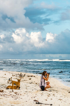 Cheerful millennial photographer taking pictures of sea on her knees