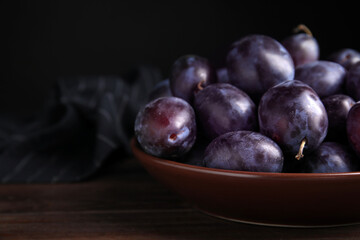 Delicious ripe plums in bowl on wooden table, space for text