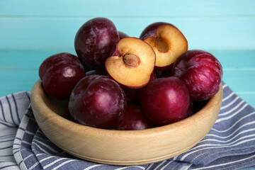 Fototapeta na wymiar Delicious ripe plums in bowl on light blue background