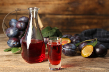 Delicious plum liquor and ripe fruits on wooden table. Homemade strong alcoholic beverage