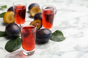 Delicious plum liquor and ripe fruits on white table. Homemade strong alcoholic beverage