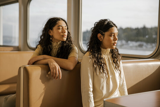 two fashionable women sitting at booth table on a ferry looking out window