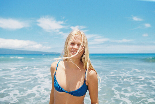 Blonde girl in blue bikini at sunshiney beach in summer with sunglasses and rainbow towel