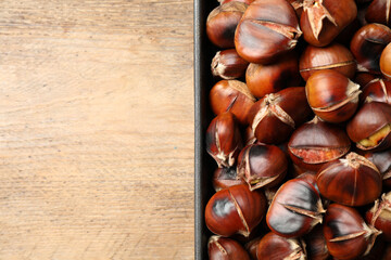 Delicious roasted edible chestnuts in baking dish on wooden table, top view. Space for text
