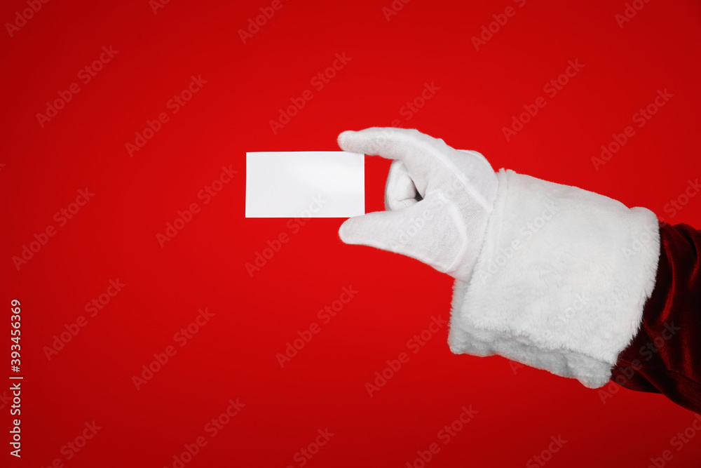 Wall mural santa claus holding blank card on red background, closeup of hand. space for text