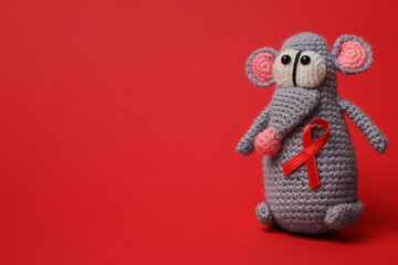 Cute knitted toy mouse with ribbon on red background, space for text. AIDS disease awareness