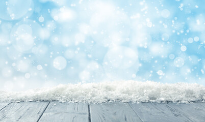 Wooden surface with snow against light blue background, bokeh effect