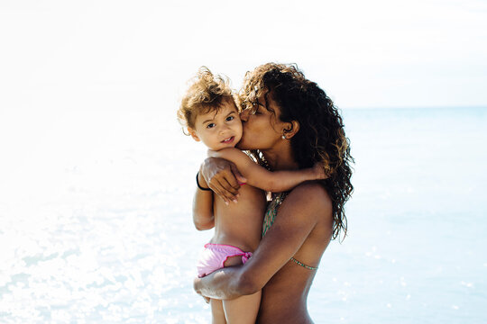 Ethnic female kissing daughter near sea