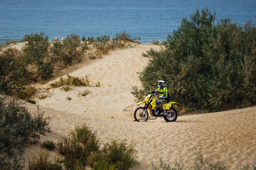 off-road motorcycle enduro motocross rider on sand dune, blue sea background