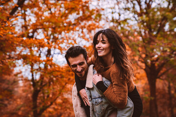 a woman on the shoulders of a man in the middle of a park with the colors of autumn