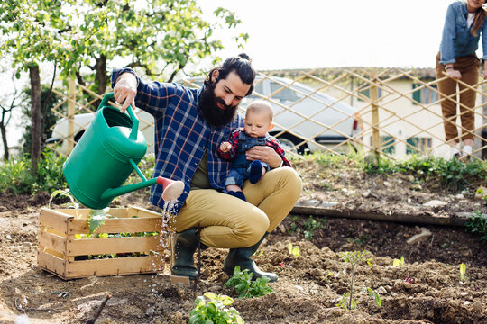 Father with baby watering plants in yard