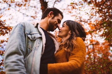 a man and a woman hugging each other in the middle of a park with autumn colors
