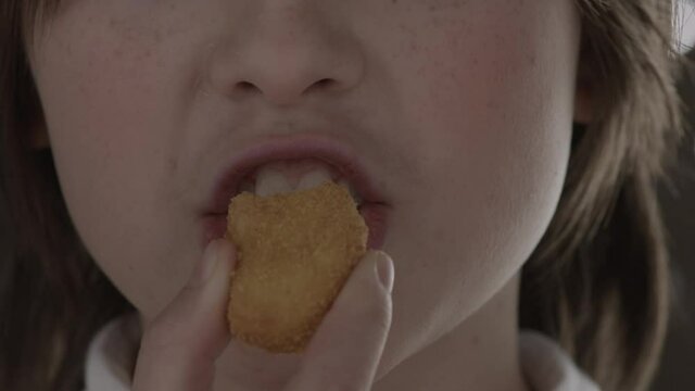 Close-up of unidentified teenage girl biting off a nugget and chewing it rather nodding her head. Concept of a favorite teenage meal. Slow motion