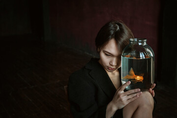 Asian girl with an aquarium fish in a dark room.