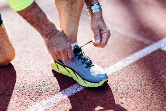 Crop senior sportsman tying shoelaces on track