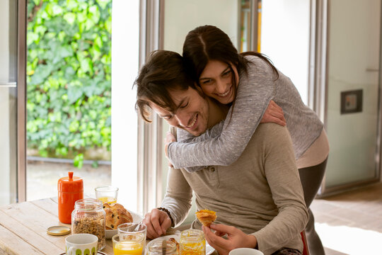 Happy woman hugging boyfriend during breakfast