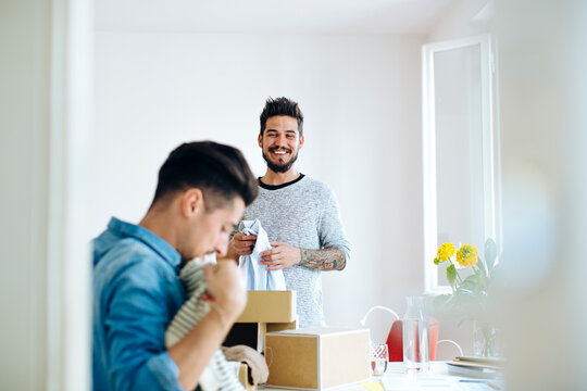 Happy ethnic boyfriends unpacking delivered clothes