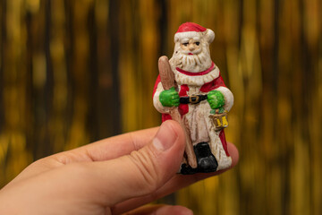 Obraz premium Woman hand holding a Santa Claus figurine on golden background. Christmas decoration