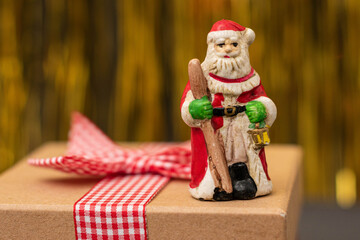 Santa Claus figurine on a christmas present with golden background. Christmas decoration