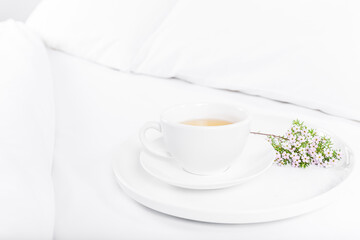 White cup of tea and flowers on the bed, white sheets. Copy space, white background.