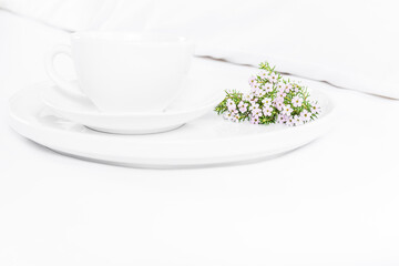 White cup of tea and flowers on the bed, white sheets. Copy space, white background.