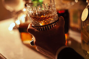 Young man's cropped hand holding a whisky glass.