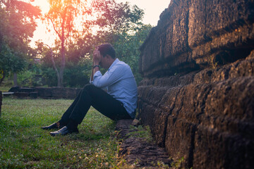 Naklejka na ściany i meble Asia you man sitting alone.He sitting alone beside old wall.man very sad and depressed.sad,alone,suicide,despair,sickness,photo health and disappointment concept.