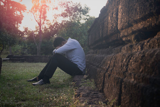 Asia you man sitting alone.He sitting alone beside old wall.man very sad and depressed.sad,alone,suicide,despair,sickness,photo health and disappointment concept.