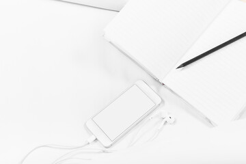 Naklejka premium Notebook, pencil, Smartphone, and earphones, on the bed, white sheets. White background, copy space, mockup.