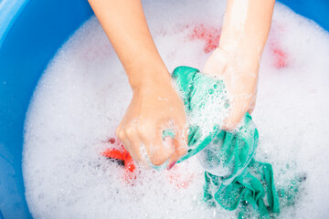 Fototapeta premium Closeup young Asian woman use hands washing color clothes in basin with detergent have soapy bubble water, studio shot background, laundry concept