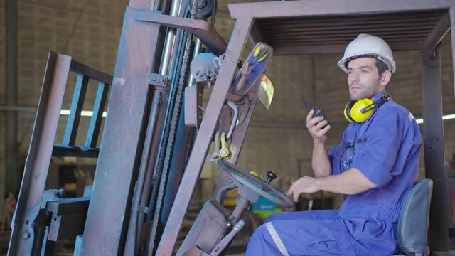 Concentrated forklift caucasian driver operating machine and holding hand on steering wheel  radio comminication operate teamwork with transportation of goods cargo in factory warehouse workshop.