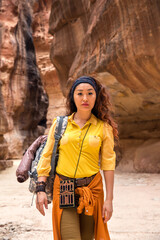 A beautiful girl in a yellow shirt and a backpack walks along the bottom of a canyon in the desert