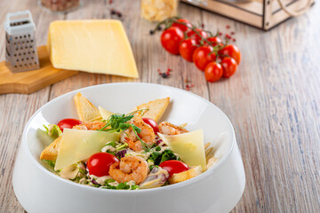 plate with salad of shrimps and cheese with cherry tomatoes on wooden background, close view 