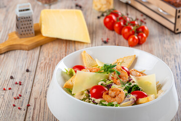 plate with salad of shrimps and cheese with cherry tomatoes on wooden background, close view 