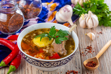 bowl with turkey soup and red peppers with garlic on wooden background, close view 