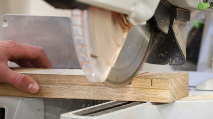 Hand holding a raw piece of timber being sawn by a fast cutting circular saw blade. Saw dust flying out. Industrial workplace manual vocation skills concept.