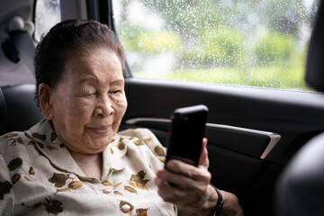 Very old Asian passenger woman age between 80 - 90 years old traveling by the car while raining and using a video call. Cheerful retired woman in a private car portrait with copy space