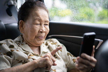 Very old Asian passenger woman age between 80 - 90 years old traveling by the car while raining and using a video call. Cheerful retired woman in a private car portrait with copy space