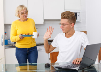 Annoyed young guy refusing cookies that his mom offering