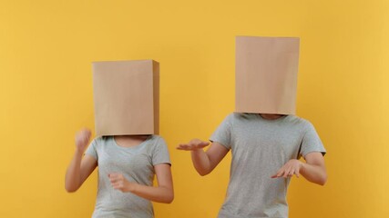 Anonymous couple cover head with paper bags doing funny dance on yellow isolated background 